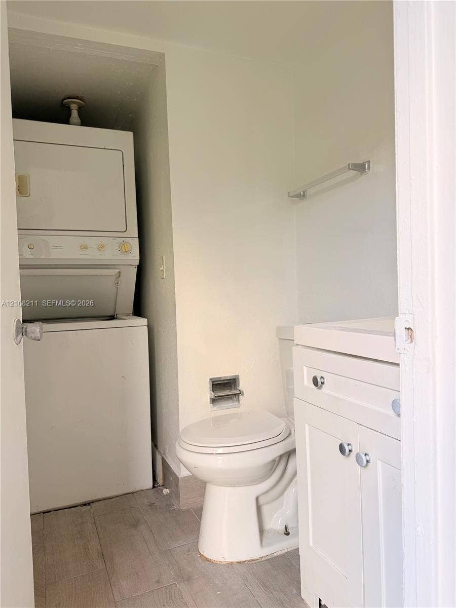 5924 NW 21st Street, #49-A, Lauderhill, Lauderhill, FL 33313 Stacked laundry unit, white vanity cabinet with a rectangular basin, ceramic toilet, and wood-finish flooring