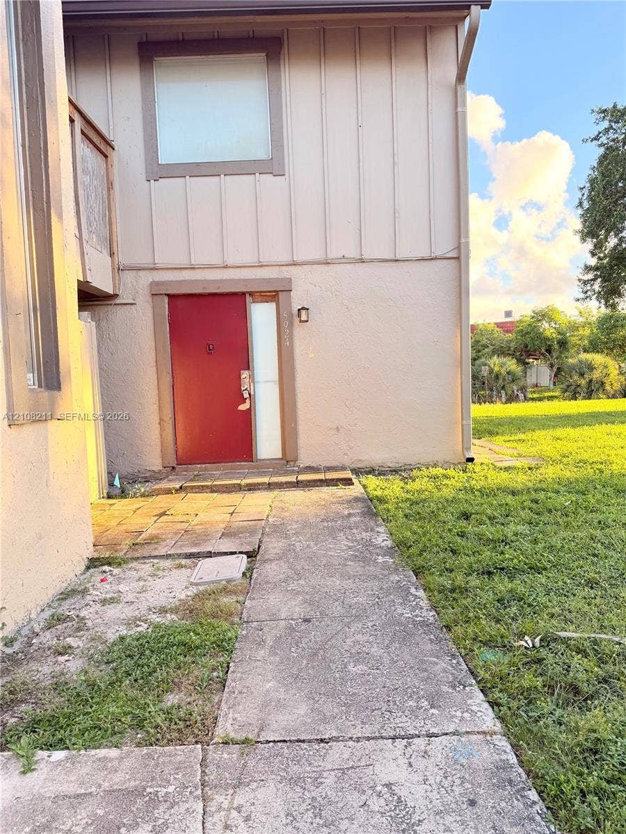 5924 NW 21st Street, #49-A, Lauderhill, Lauderhill, FL 33313 Exterior featuring vertical board-and-batten siding, stucco finish, a red entry door with sidelight, and a concrete paver walkway