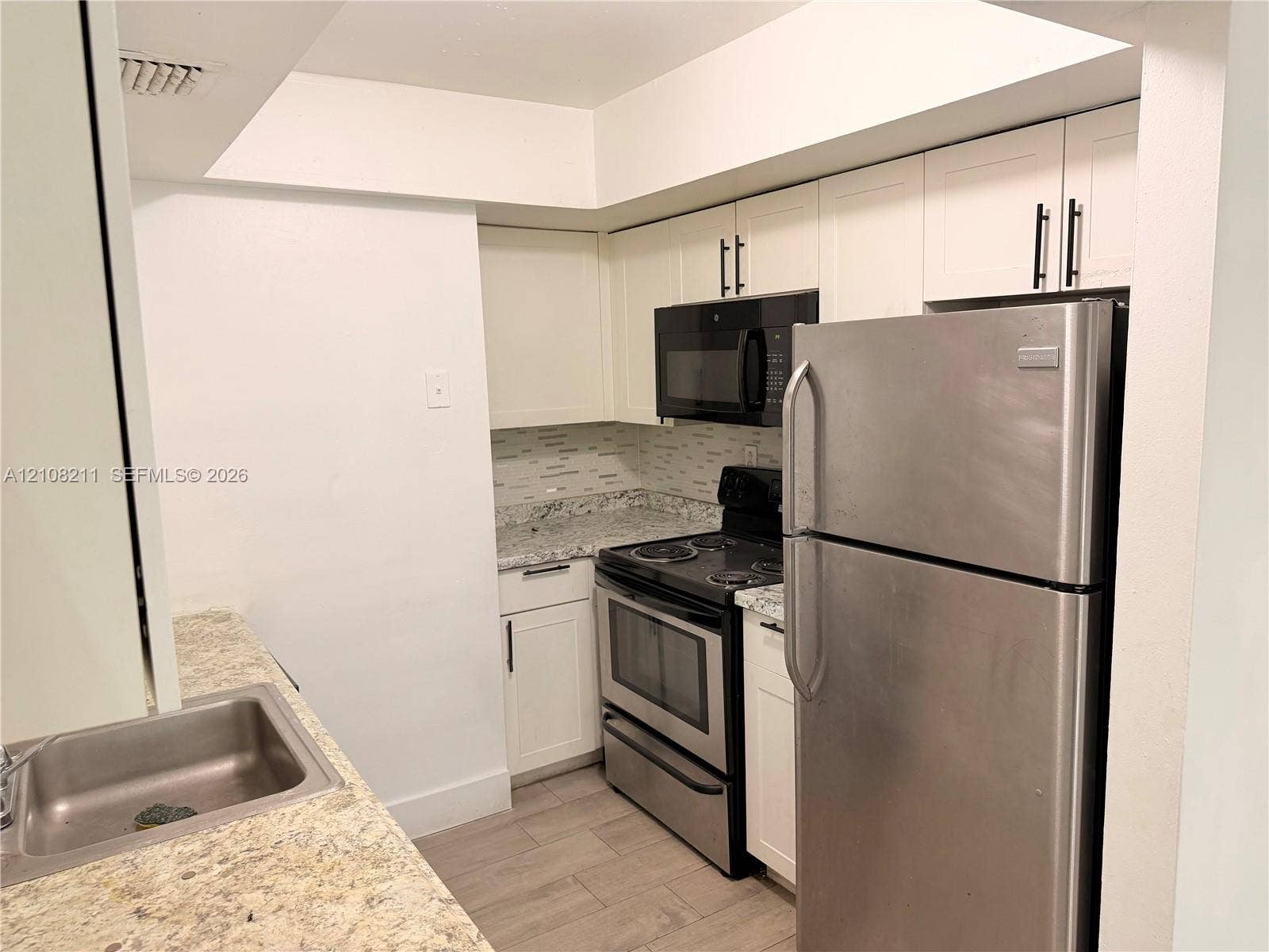 5924 NW 21st Street, #49-A, Lauderhill, Lauderhill, FL 33313 Kitchen featuring white cabinetry with matte black hardware, stone-patterned countertops, stainless steel appliances, a tile backsplash, and wood-finish flooring