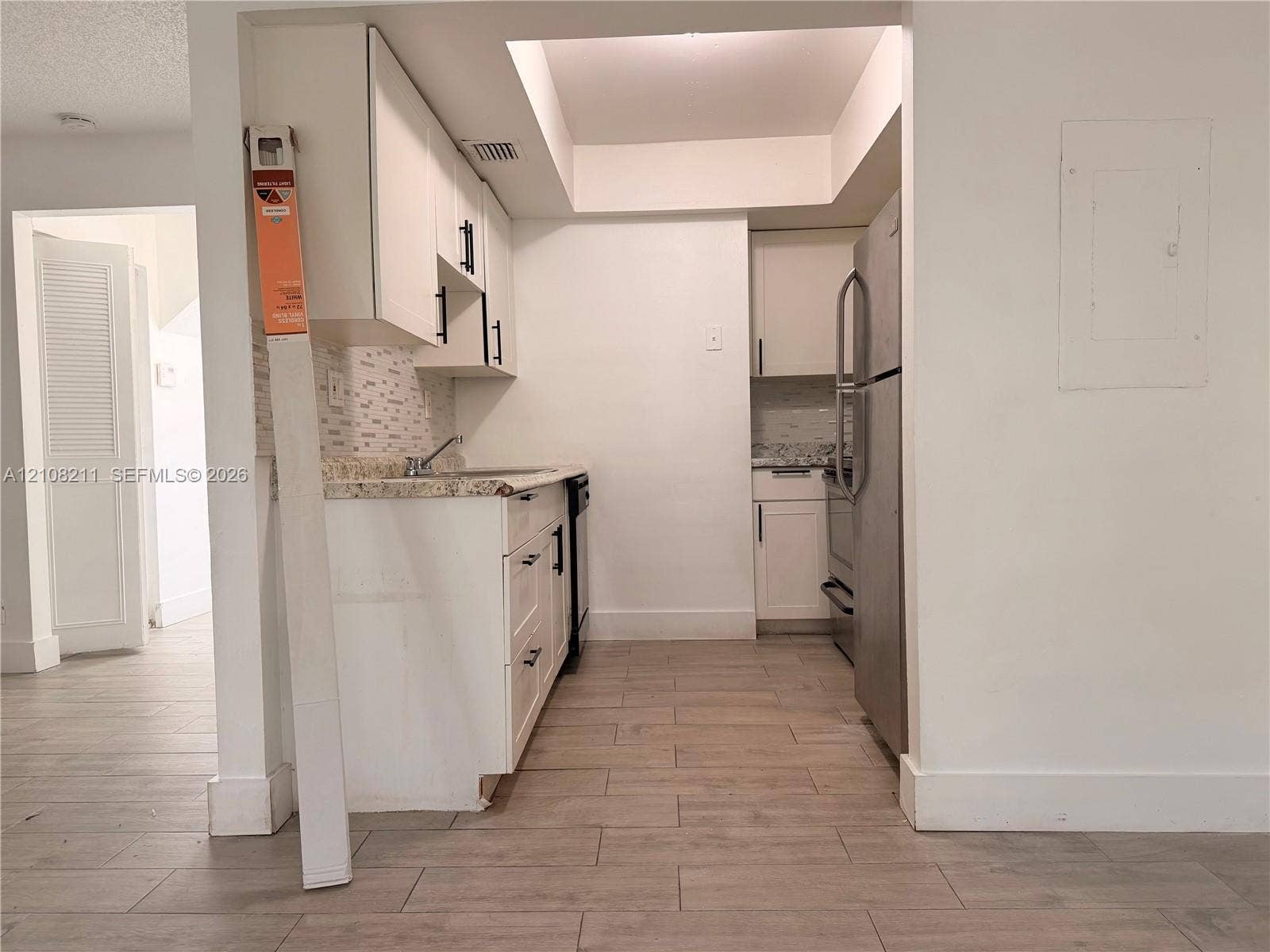 5924 NW 21st Street, #49-A, Lauderhill, Lauderhill, FL 33313 Kitchen featuring white cabinetry with matte black hardware, stone-patterned countertops, a tiled backsplash, stainless steel refrigerator, and wood-finish flooring