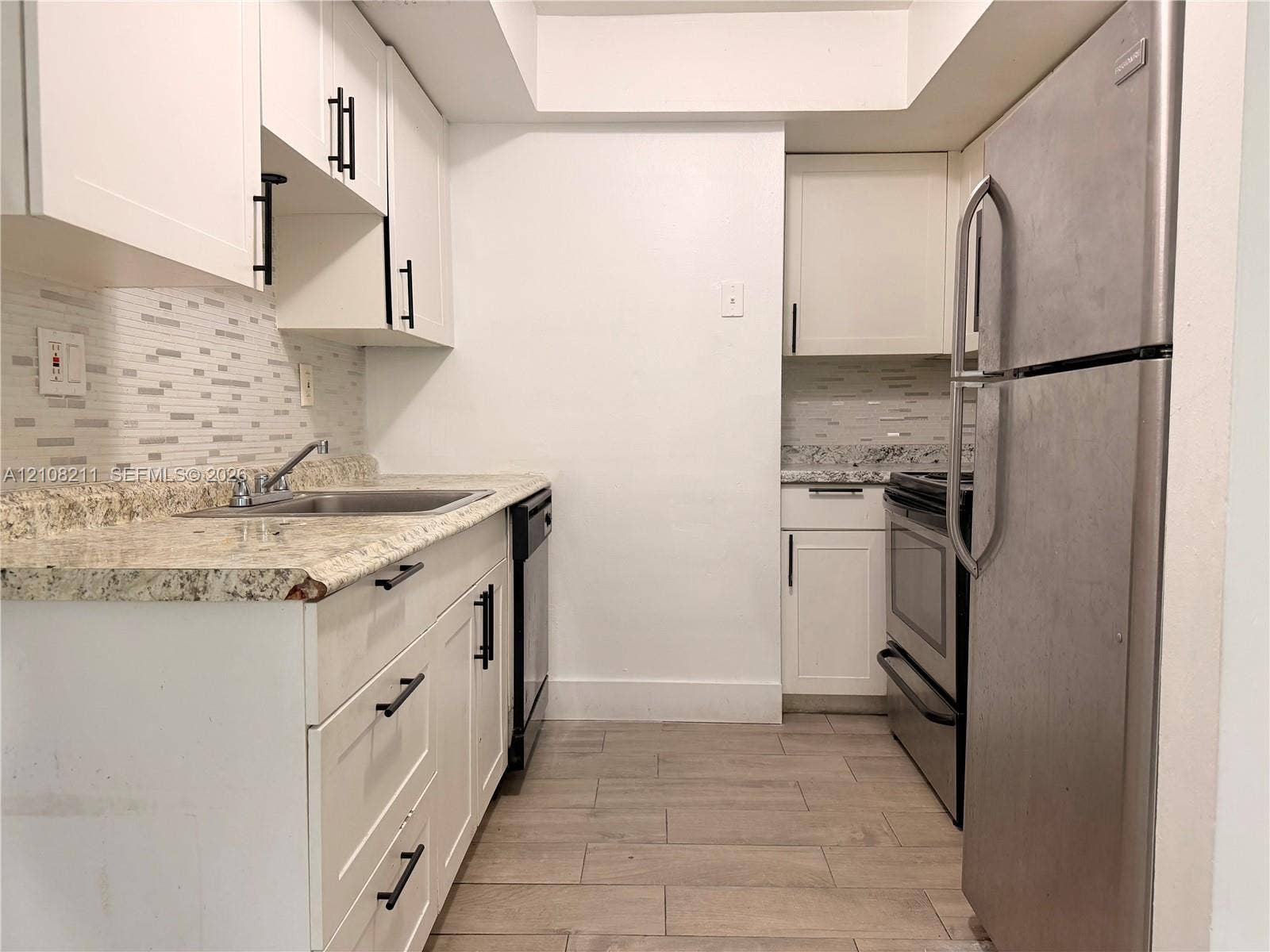 5924 NW 21st Street, #49-A, Lauderhill, Lauderhill, FL 33313 Kitchen featuring white shaker-style cabinetry, stone-surface countertops, mosaic tile backsplash, stainless steel appliances, and wood-finish flooring