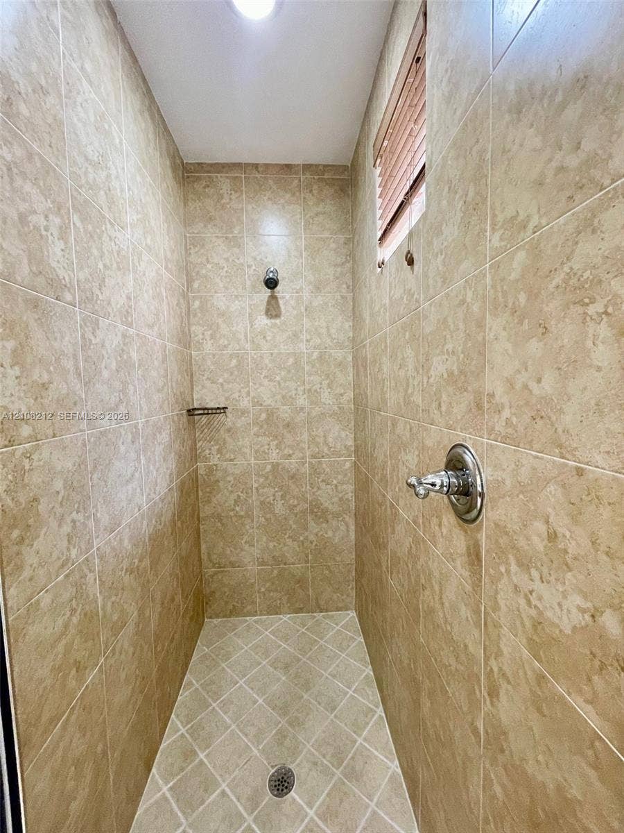 Sunrise, FL 33323 Shower stall featuring full-height neutral-toned tile walls, a diamond-patterned tile floor, recessed lighting, and integrated metal shower fixtures