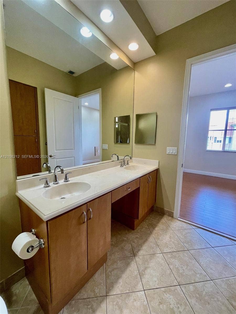 Sunrise, FL 33323 Dual-sink vanity with light-tone cabinetry, solid surface countertop, inset rectangular mirrors, recessed ceiling lighting, and ceramic tile flooring