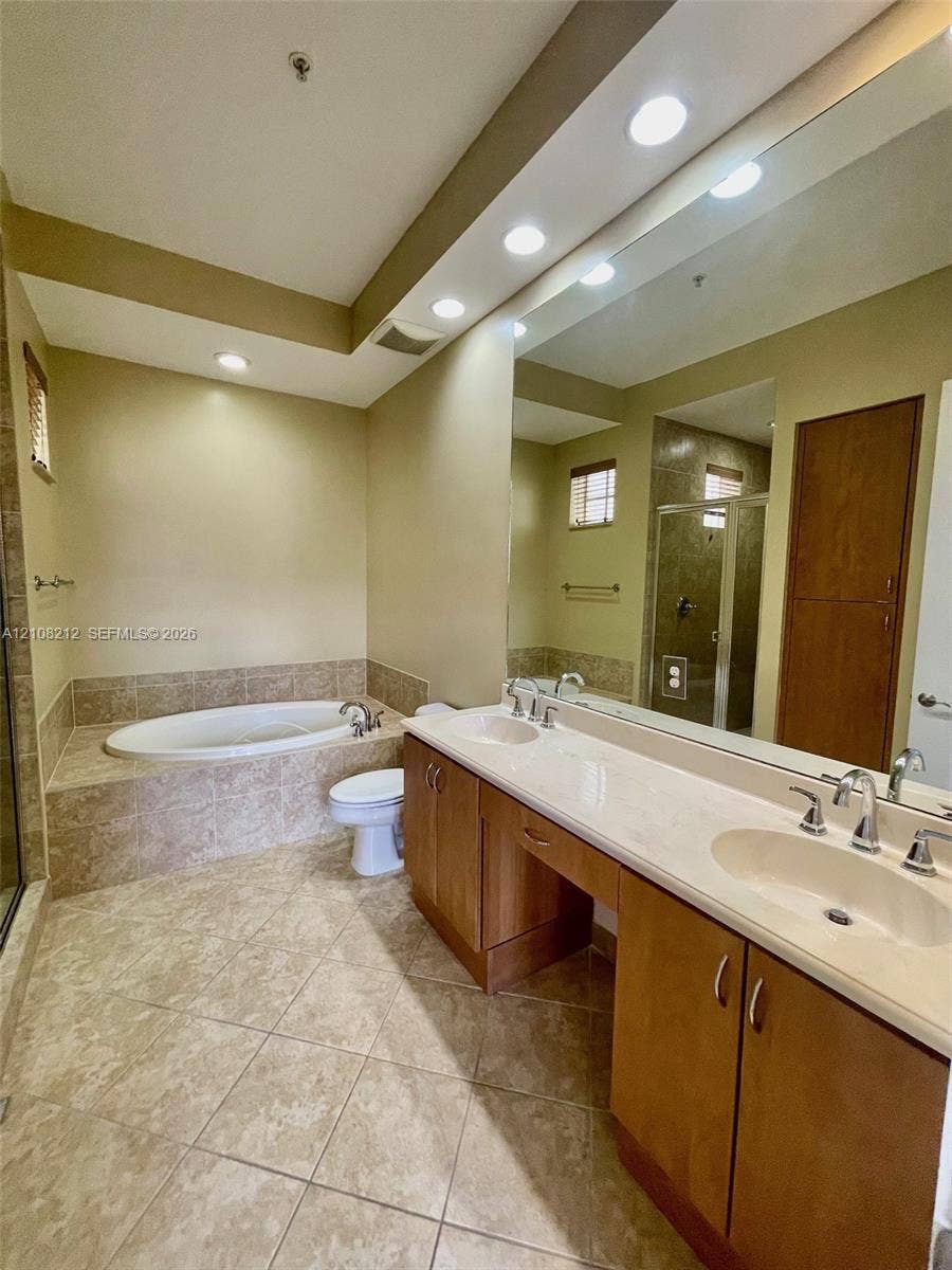 Sunrise, FL 33323 Dual-sink vanity with stone-finish countertop, soaking tub surrounded by tile, full-width mirror, recessed lighting, and tile flooring