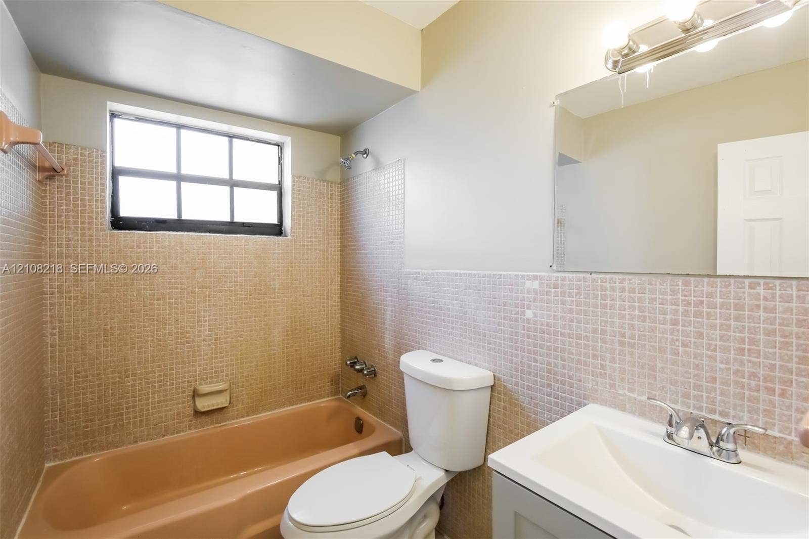 Bathroom featuring a tiled bathtub surround, wall-mounted mirror, vanity with integrated basin, polished metal faucet, and window with grid muntins