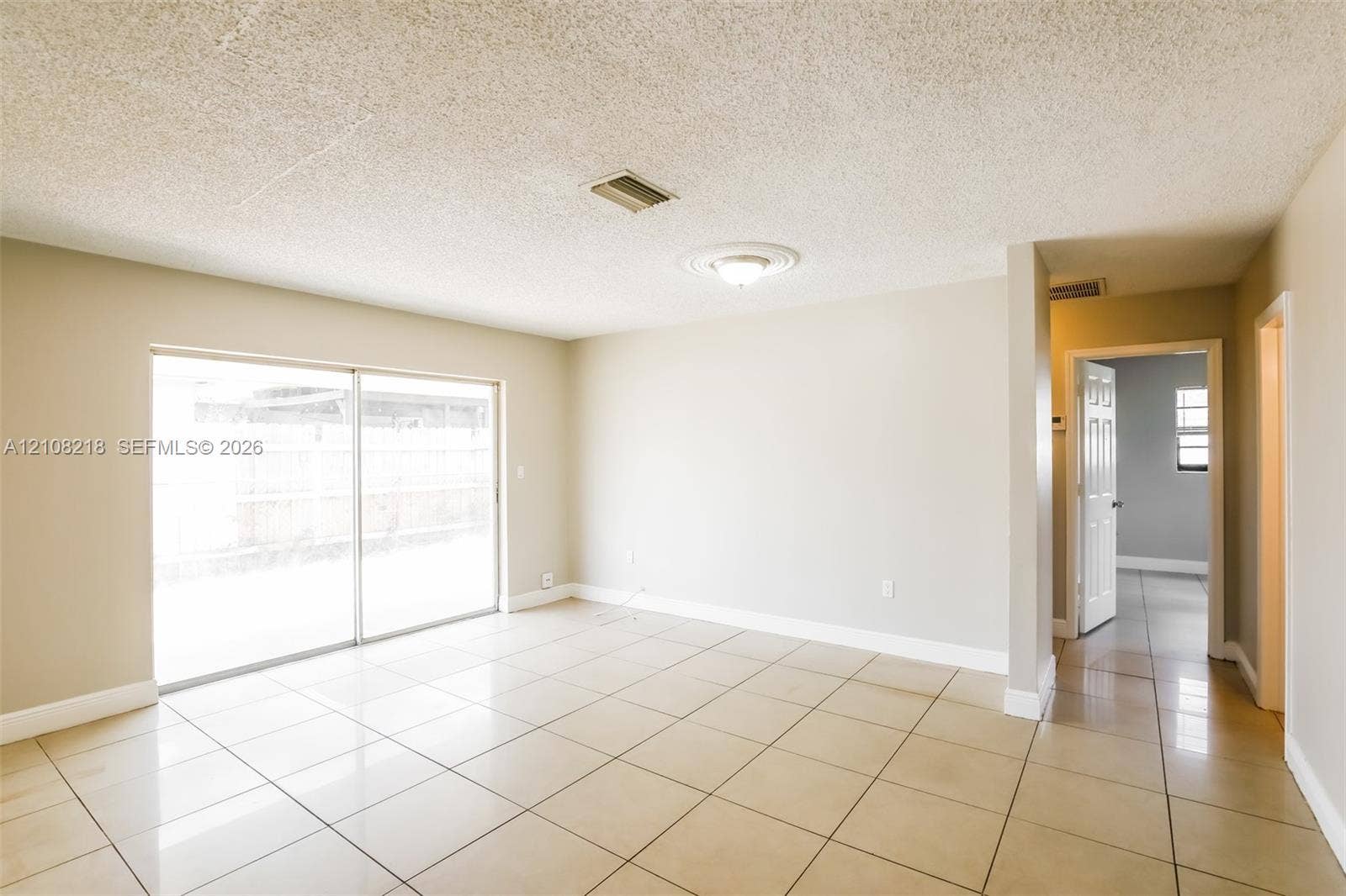 Neutral-toned interior space featuring light-colored ceramic tile flooring, sliding glass doors, a ceiling-mounted light fixture with medallion detail, and textured ceiling finish