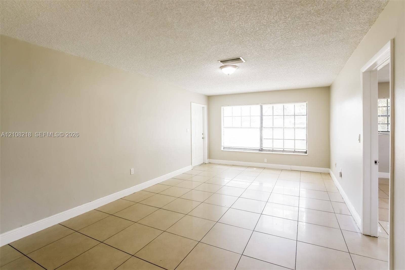 Neutral-toned interior space featuring ceramic tile flooring, a large multi-pane window, and a central flush-mount ceiling light fixture