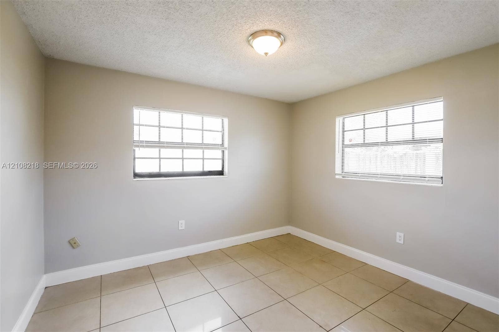 Room featuring large-format neutral floor tile, two multi-pane windows, and a flush-mount ceiling fixture