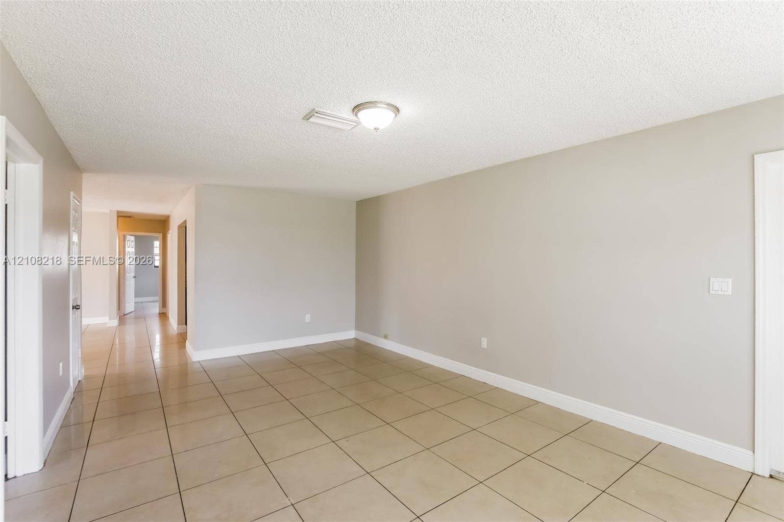 Neutral-toned interior space featuring light-colored square floor tiling, crisp white door frames, and a flush-mount ceiling light fixture