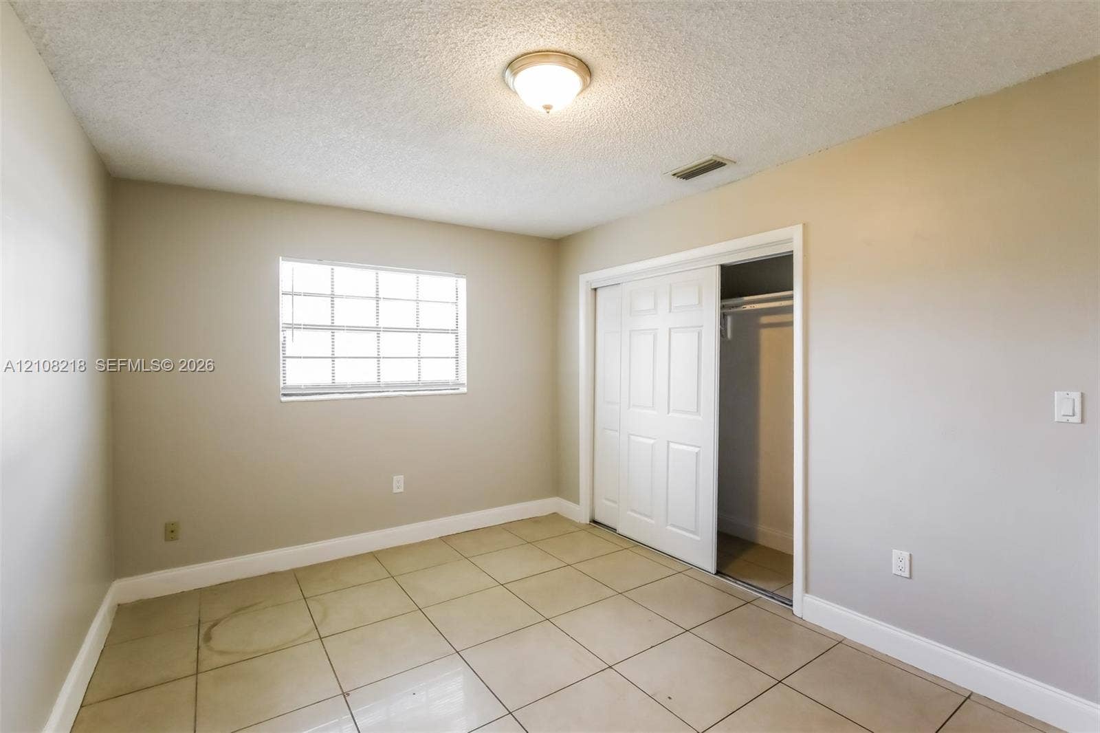 Neutral-toned room featuring large-format square tile flooring, a multi-pane window, and a built-in closet with white paneled sliding doors