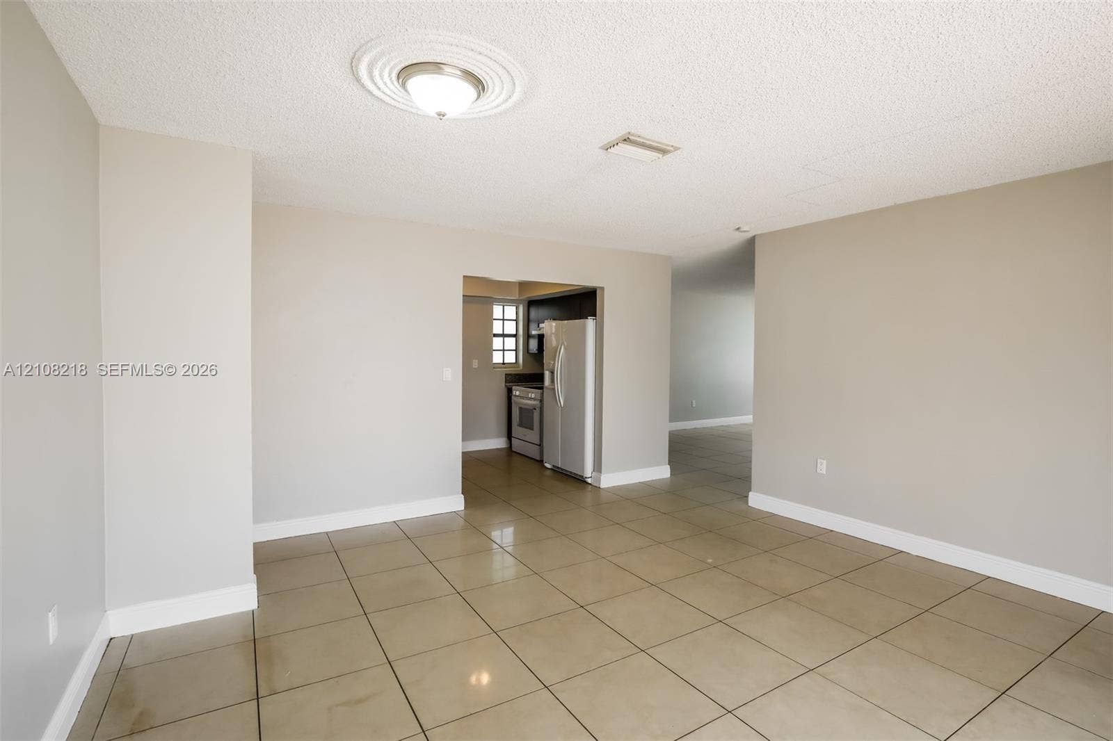 Neutral-toned interior featuring large-format tile flooring, a ceiling medallion with a flush-mount light fixture, and visible kitchen cabinetry with stainless steel appliances