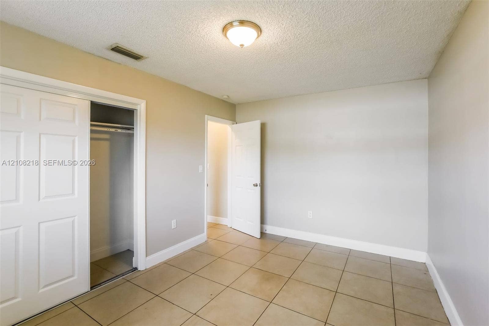 Neutral-toned room featuring large-format square tile flooring, a sliding bypass closet door, a solid-panel door, and a flush-mount ceiling light fixture