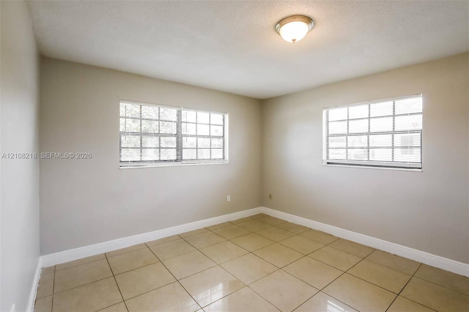 Room featuring neutral wall paint, polished tile flooring, dual windows with grid detailing, and a flush-mount ceiling light fixture