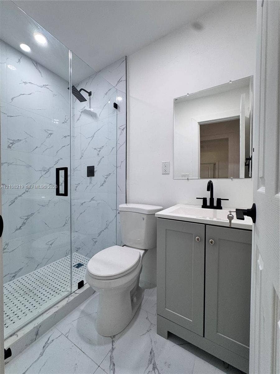 2381 NW 153rd Street, #2353, Miami Gardens, Miami Gardens, FL 33054 Walk-in shower with stone-finish tile surround and frameless glass door, gray Shaker-style vanity, matte black plumbing fixtures, and stone-finish floor tiling