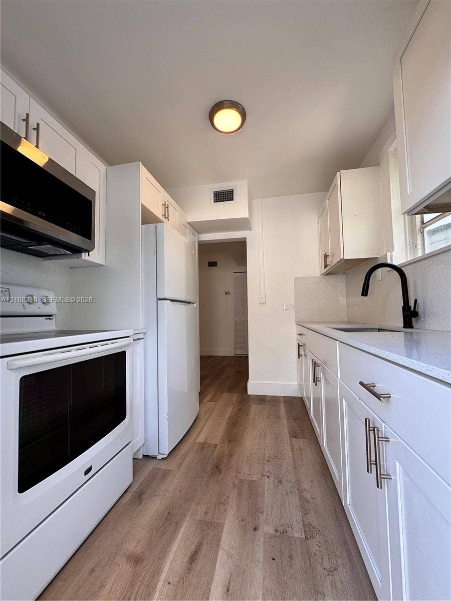 2381 NW 153rd Street, #2353, Miami Gardens, Miami Gardens, FL 33054 Kitchen featuring white shaker-style cabinetry, solid-surface countertops, wood-finish flooring, a stainless steel microwave, and a matte black faucet