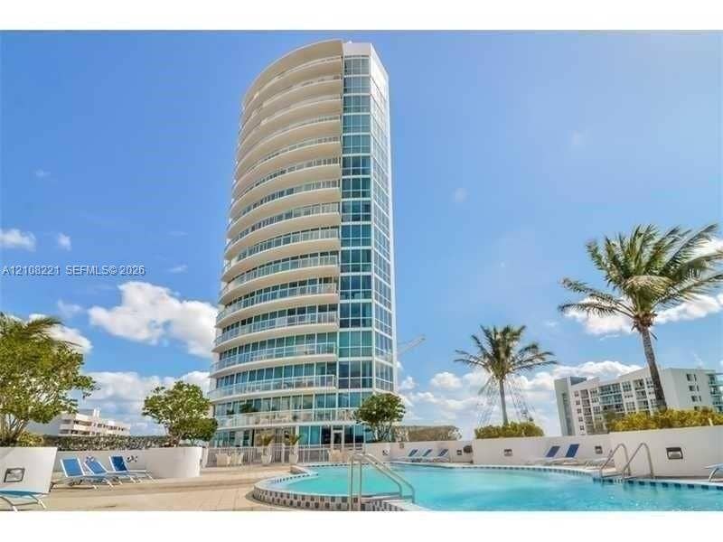 High-rise residential tower featuring a curved glass facade, floor-to-ceiling windows, and private balconies, complemented by a ground-level swimming pool and landscaped hardscaping