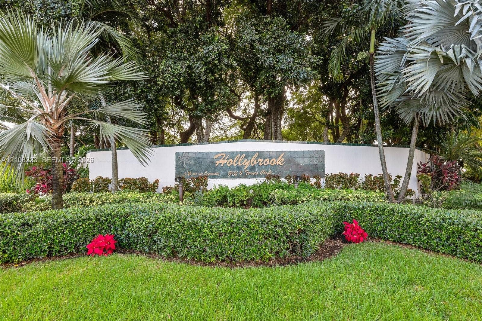 311 S Hollybrook Drive, #309, Pembroke Pines, FL 33025 Hollybrook community entrance featuring manicured hedges, mature palm trees, and professional landscaping