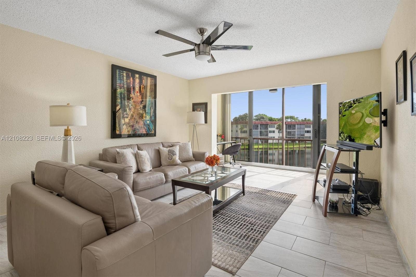 311 S Hollybrook Drive, #309, Pembroke Pines, FL 33025 Living area featuring large-format tile flooring, a central multi-blade ceiling fan, and floor-to-ceiling sliding glass doors opening to a screened balcony