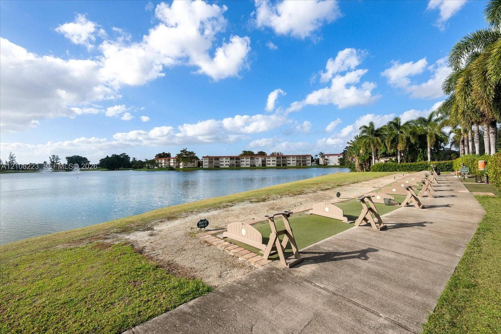 311 S Hollybrook Drive, #309, Pembroke Pines, FL 33025 Waterfront driving range featuring a concrete walkway, designated tee boxes with synthetic turf, and mature palm trees