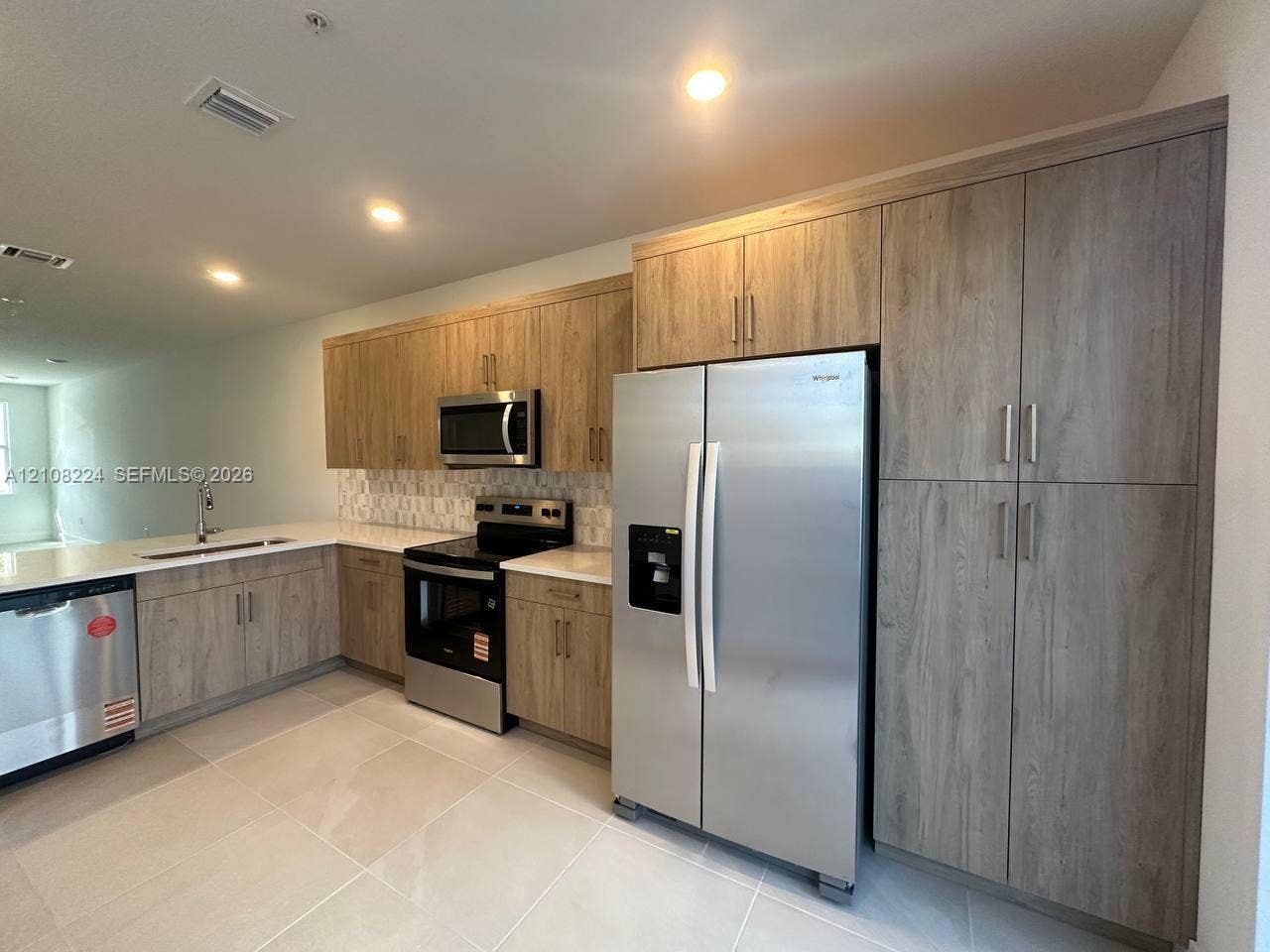 17183 SW 2nd Circle, #17183, Pembroke Pines, Pembroke Pines, FL 33027 Kitchen featuring textured wood-finish cabinetry, stainless steel appliances, light-toned solid surface countertops, a decorative mosaic tile backsplash, and large-format floor tile