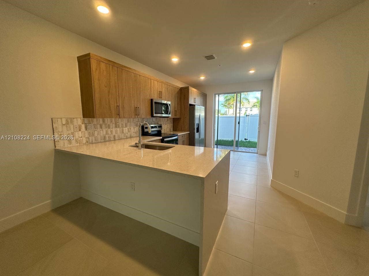 17183 SW 2nd Circle, #17183, Pembroke Pines, Pembroke Pines, FL 33027 Kitchen featuring wood-finish cabinetry, quartz countertops, a stone-tile backsplash, stainless steel appliances, and large-format tile flooring