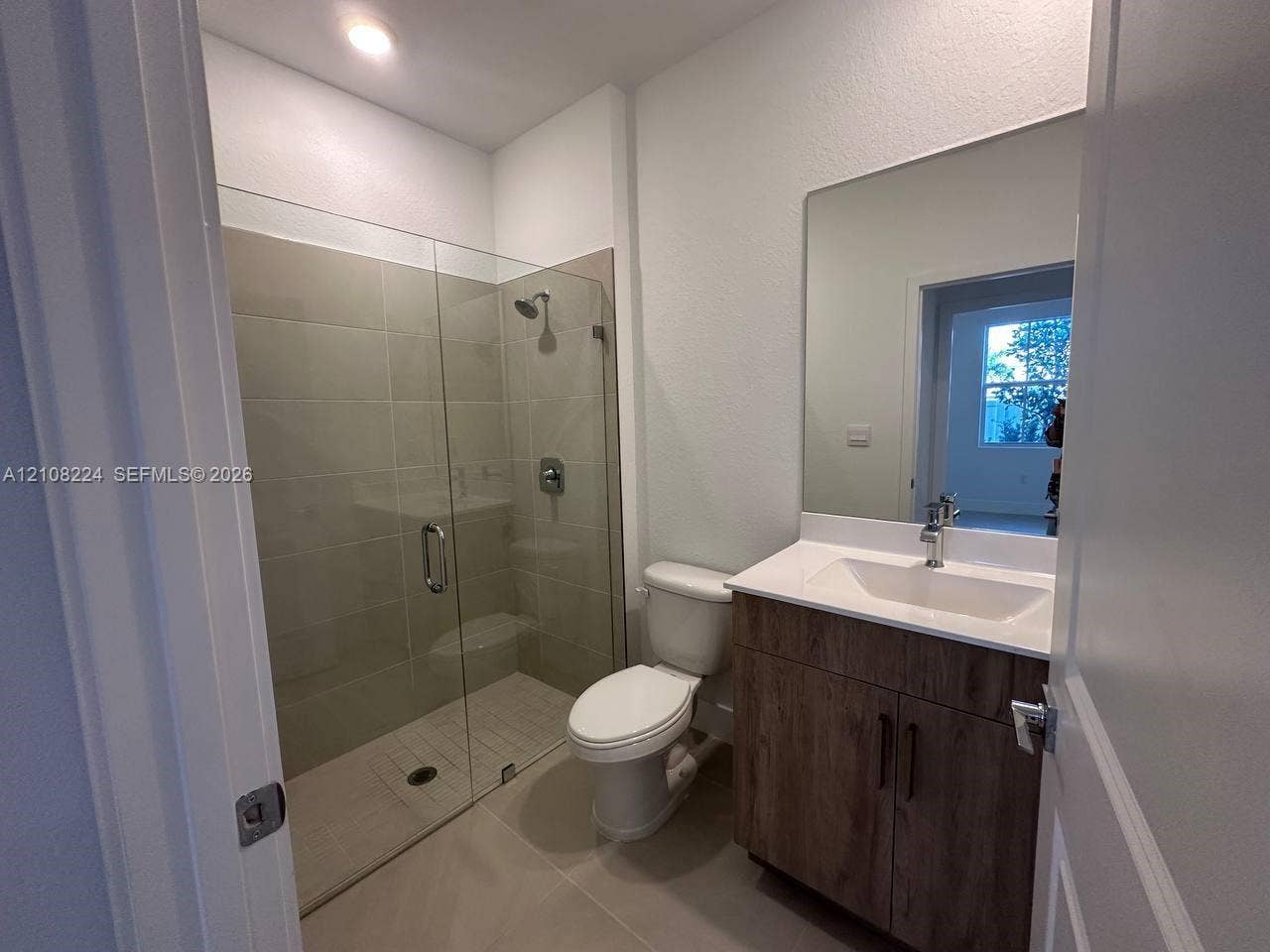 17183 SW 2nd Circle, #17183, Pembroke Pines, Pembroke Pines, FL 33027 Walk-in shower with floor-to-ceiling tile, wood-finish vanity with an integrated basin, countertop with stone-style surface, and frameless vanity mirror