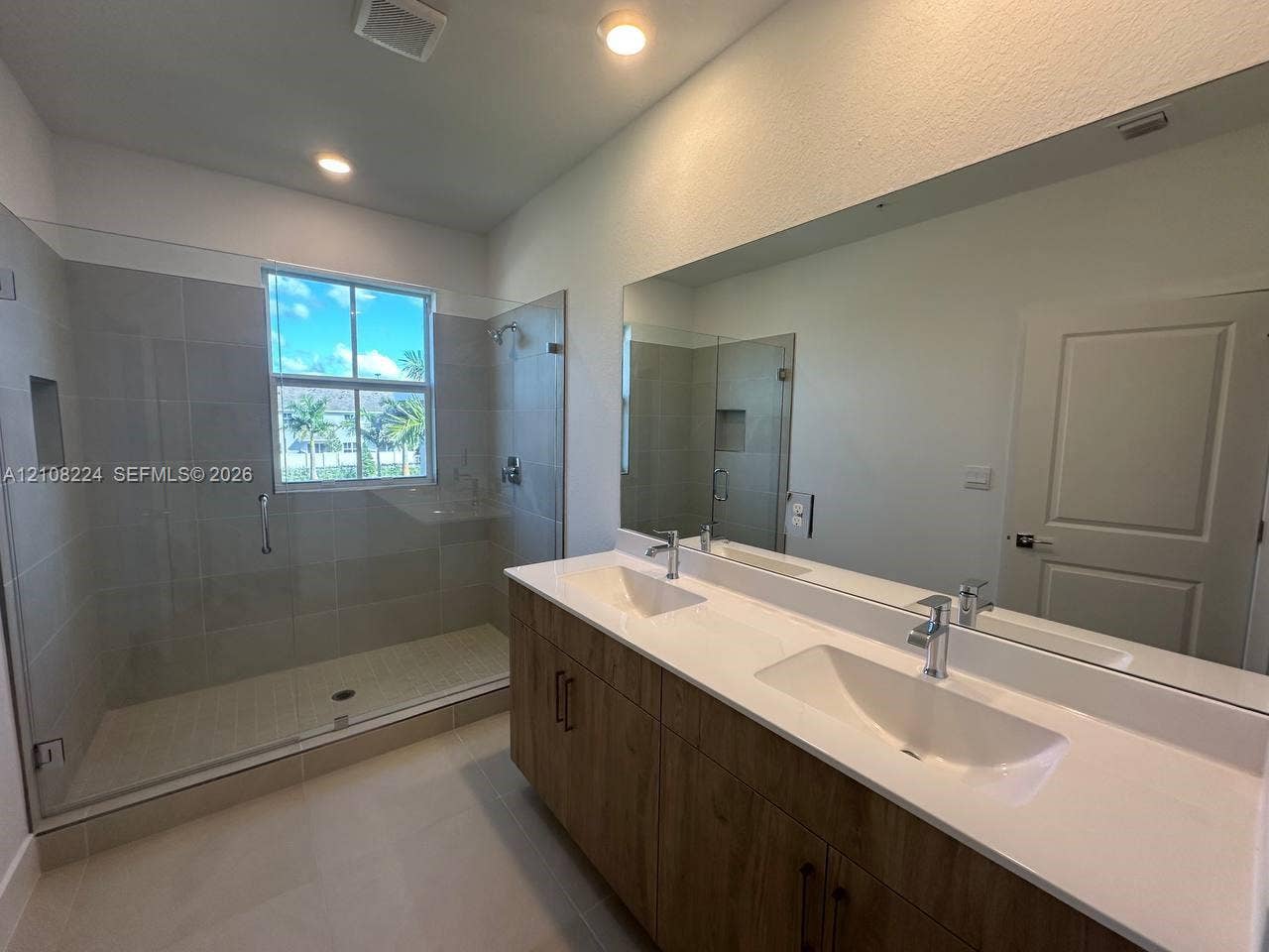 17183 SW 2nd Circle, #17183, Pembroke Pines, Pembroke Pines, FL 33027 Dual-sink vanity with a white countertop and wood-finish cabinetry, frameless glass-enclosed shower featuring tile walls, integrated shower niche, and a large wall-mounted mirror