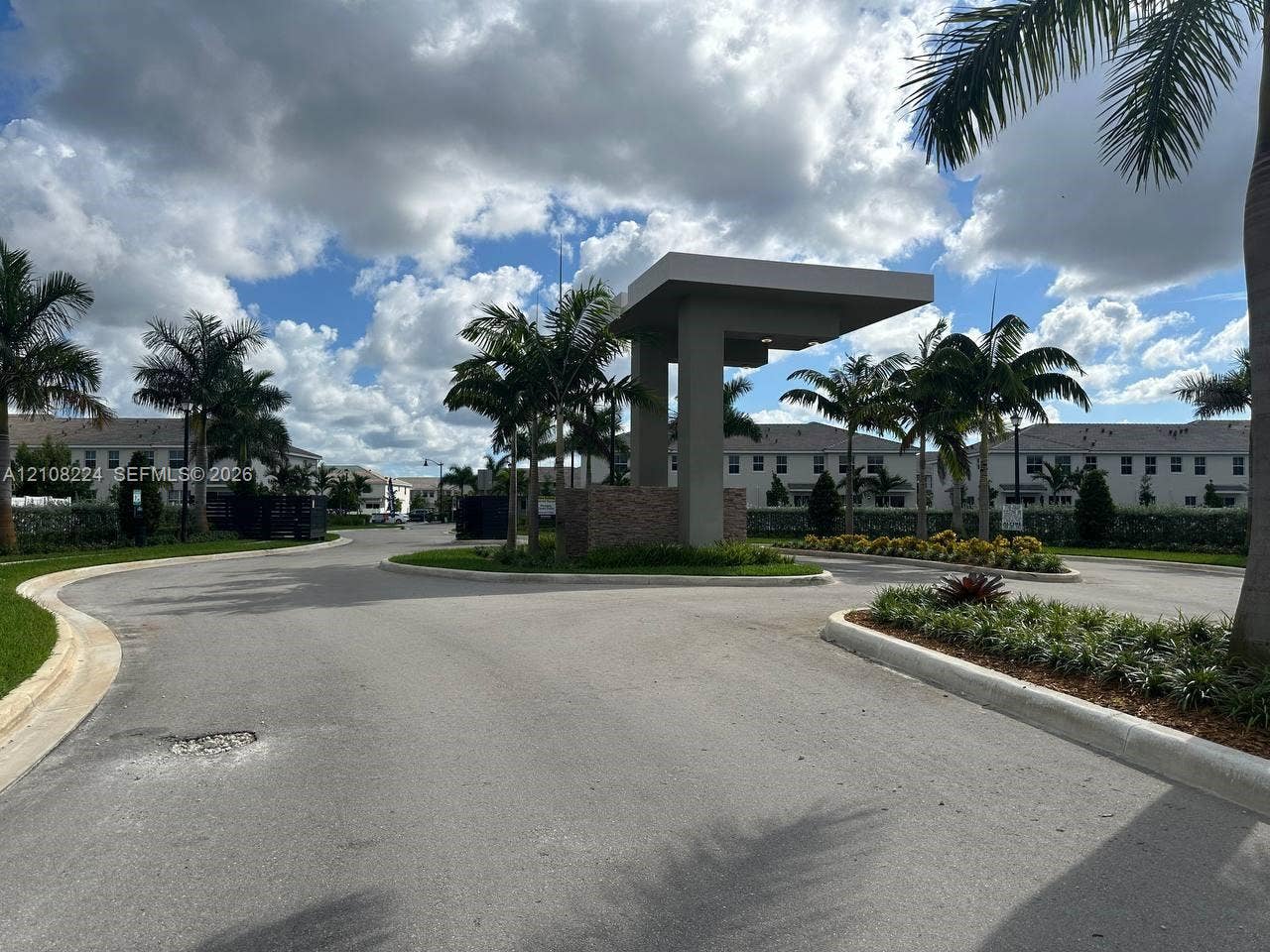 17183 SW 2nd Circle, #17183, Pembroke Pines, Pembroke Pines, FL 33027 Entryway featuring a modern geometric gatehouse, stone-veneer pillar accents, asphalt paving, and established palm landscaping