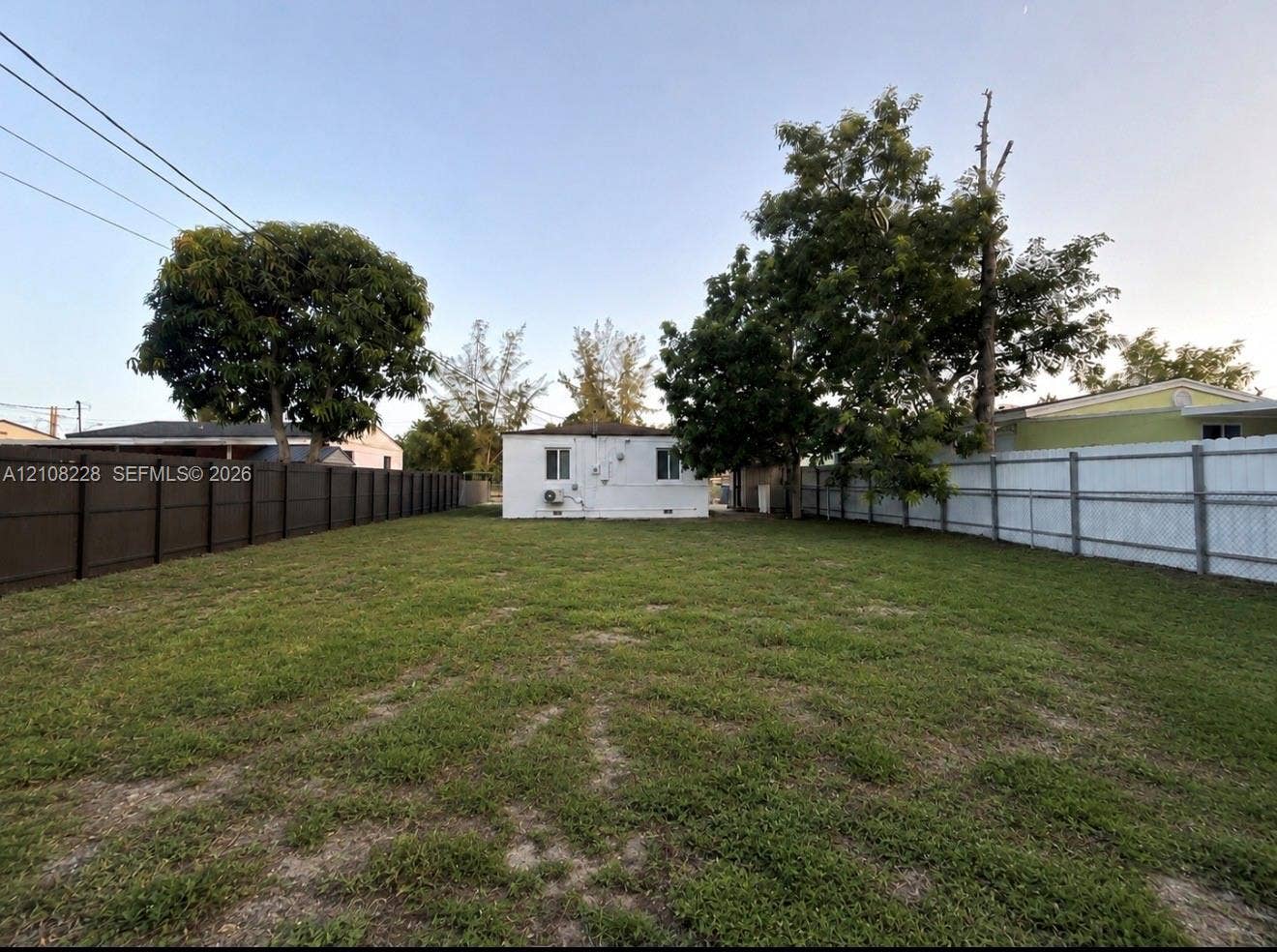 Expansive backyard featuring a large grass lawn, mature trees, and perimeter fencing