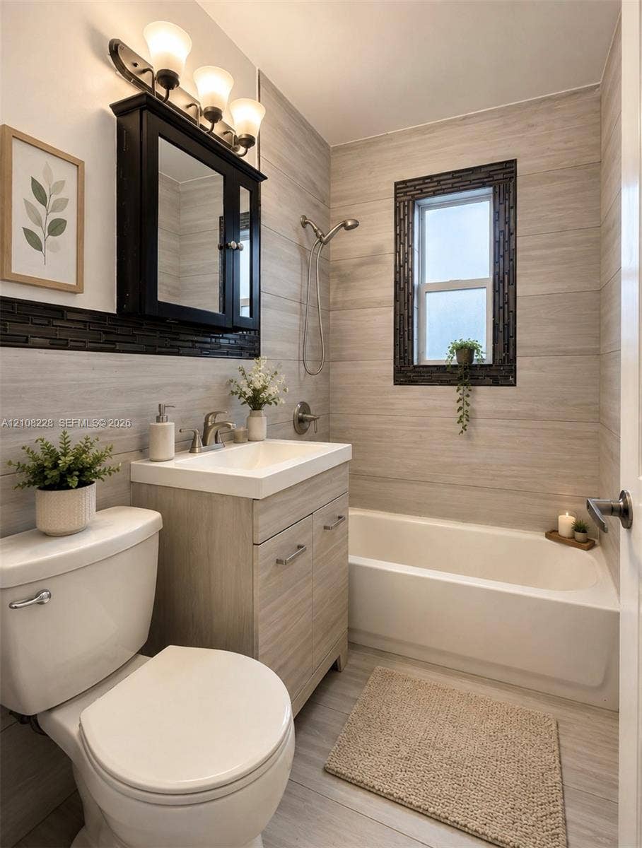 Bathroom featuring horizontal tile wall cladding, wood-finish vanity with an integrated sink, dark-framed medicine cabinet, and a tiled tub surround with a window inset