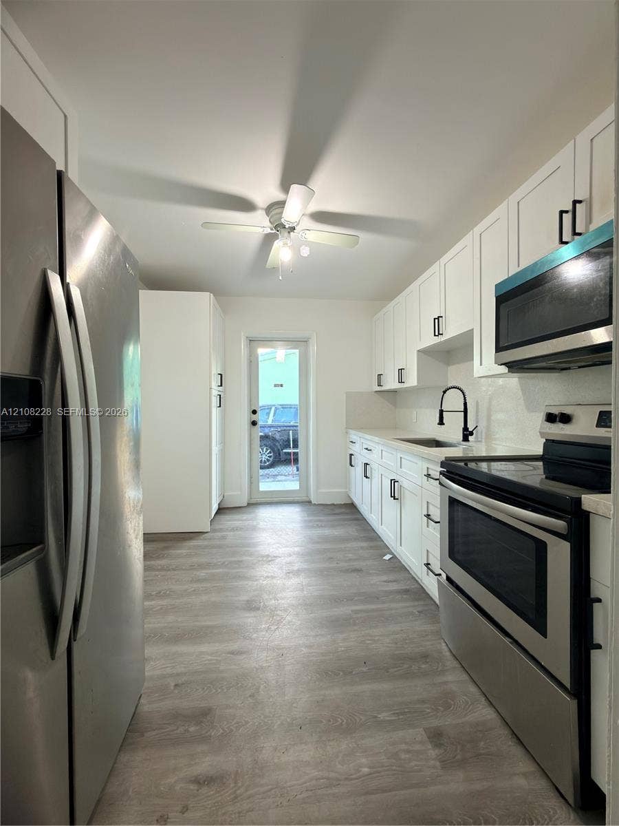 Kitchen featuring white cabinetry with matte black hardware, stainless steel appliances, wood-finish flooring, a matte black kitchen faucet, and a ceiling-mounted light fixture