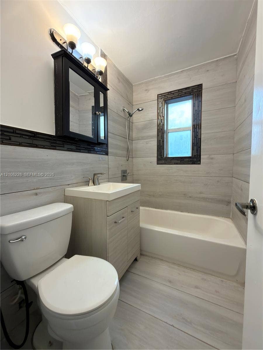 Bathroom featuring light-toned wood-finish wall and floor tile, a recessed medicine cabinet with integrated lighting, a modern vanity with an inset sink, and a tiled bathtub surround with a mosaic accent border