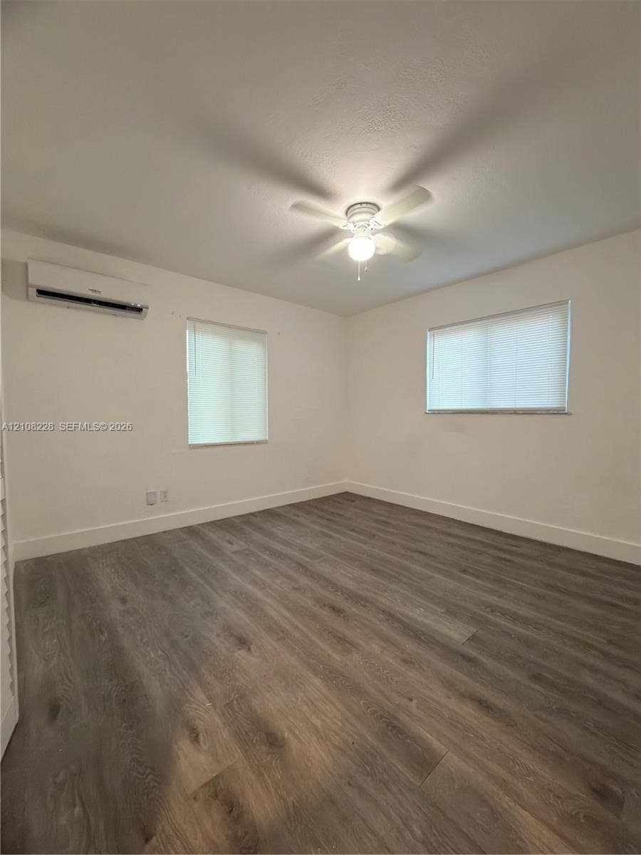 Room featuring wood-finish flooring, a wall-mounted ductless air conditioning unit, neutral walls, and a ceiling fan with integrated lighting
