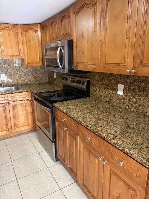 3200 Coral Springs Drive, Coral Springs, FL 33065 Kitchen featuring arched-panel wood cabinetry, speckled stone countertops, a stainless steel microwave and oven, a dual-basin stainless steel sink, and light-tone ceramic tile flooring