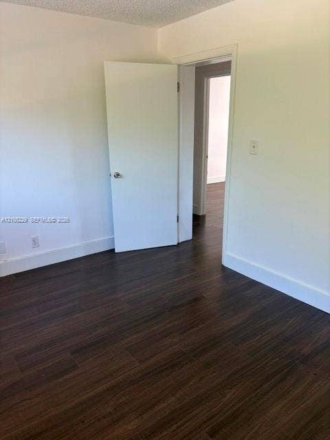 3200 Coral Springs Drive, Coral Springs, FL 33065 Interior space featuring dark wood-finish flooring, smooth white walls, and a white interior door with a metallic knob