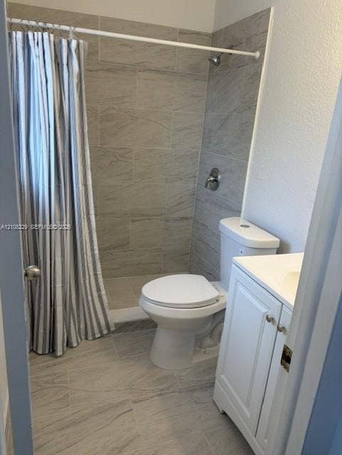 3200 Coral Springs Drive, Coral Springs, FL 33065 Bathroom featuring large-format tile flooring, a shower surround with neutral tile detailing, a white vanity cabinet, and a two-piece toilet