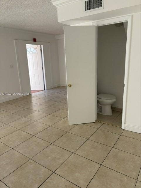 3200 Coral Springs Drive, Coral Springs, FL 33065 Neutral tile flooring throughout an interior space featuring a solid-core entry door with window pane detailing and a private water closet with a standard porcelain commode