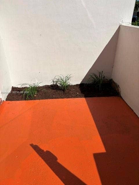 3200 Coral Springs Drive, Coral Springs, FL 33065 Paved patio featuring terra-cotta colored hardscaping and a dedicated soil garden bed with established ornamental grasses enclosed by smooth white stucco walls