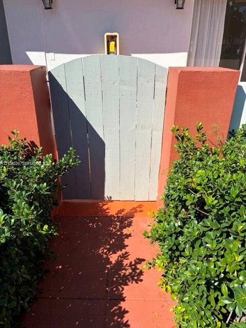 3200 Coral Springs Drive, Coral Springs, FL 33065 Arched wooden pedestrian gate flanked by stucco-finished masonry pillars and mature greenery