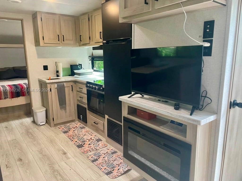 573 Mokena Drive, #1, Miami Springs, Miami Springs, FL 33166 Kitchen featuring light wood-finish cabinetry, countertop with stone-patterned surfacing, integrated oven and stovetop, wood-finish flooring, and a built-in electric fireplace