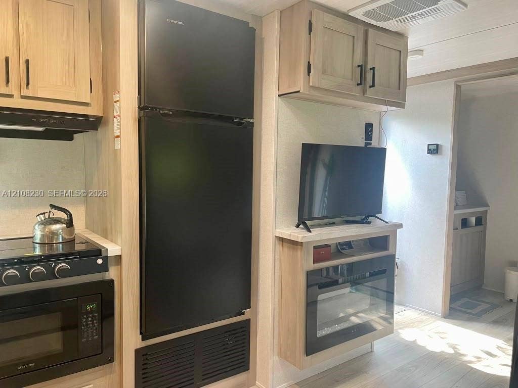 573 Mokena Drive, #1, Miami Springs, Miami Springs, FL 33166 Kitchen area featuring light-toned cabinetry, a black full-size refrigerator, a built-in microwave, and a black cooktop