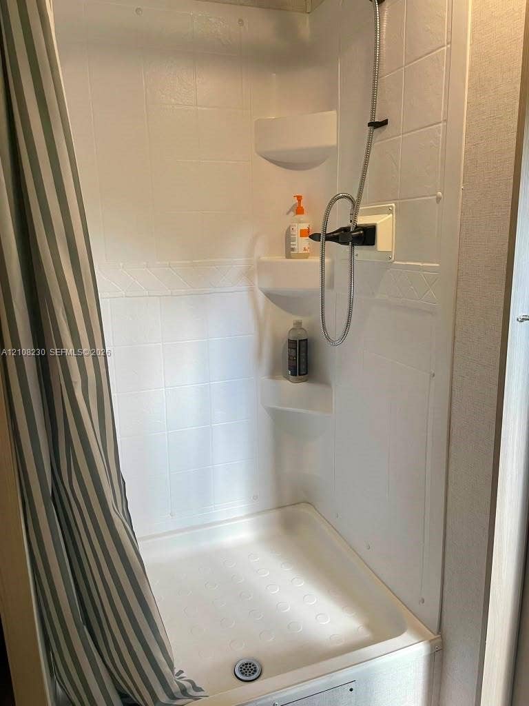 573 Mokena Drive, #1, Miami Springs, Miami Springs, FL 33166 Shower enclosure featuring white wall panels with a textured tile pattern, three integrated corner shelves, a molded shower pan, and a handheld shower fixture
