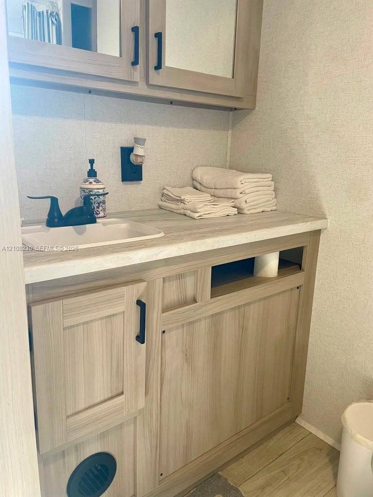 573 Mokena Drive, #1, Miami Springs, Miami Springs, FL 33166 Vanity with wood-finish cabinetry, solid-surface countertop, integrated sink, matte black faucet, and mirrored medicine cabinet