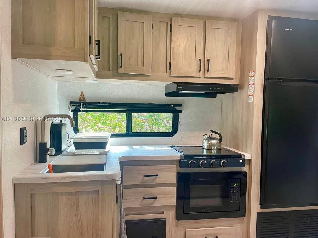 573 Mokena Drive, #1, Miami Springs, Miami Springs, FL 33166 Kitchen featuring wood-finish cabinetry, light-toned countertops, a matte black faucet, and built-in black appliances including a stove, microwave, and refrigerator