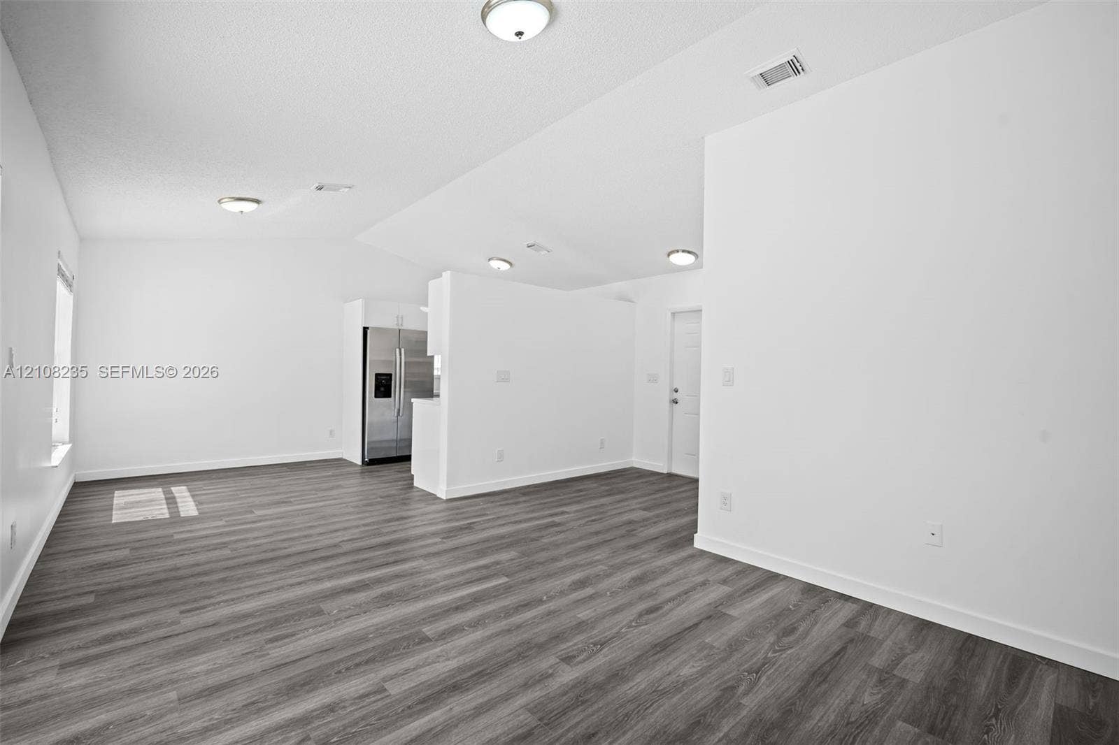 12752 SW 250th Terrace, Homestead, FL 33032 Vaulted ceiling with flush-mount lighting and wood-finish flooring throughout the open-concept space, featuring a stainless steel side-by-side refrigerator