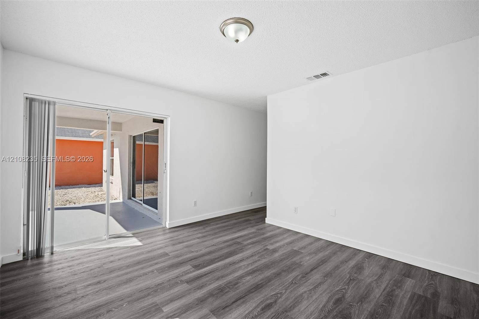 12752 SW 250th Terrace, Homestead, FL 33032 Interior space featuring wood-finish flooring, white walls, flush-mount ceiling lighting, and sliding glass doors with vertical blinds leading to a paved patio area