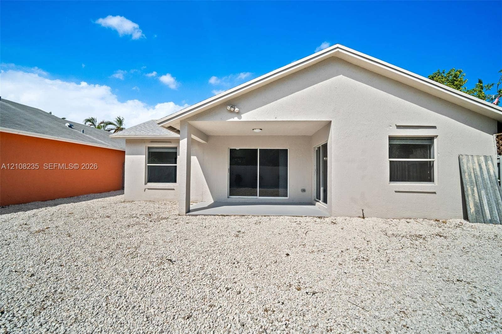 12752 SW 250th Terrace, Homestead, FL 33032 Rear exterior elevation featuring a stucco facade, covered patio, sliding glass doors, and gravel landscaping
