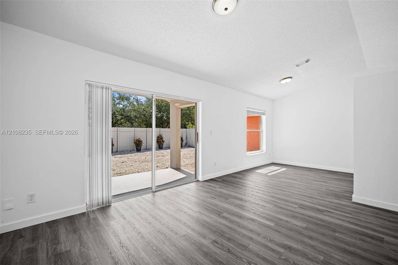 12752 SW 250th Terrace, Homestead, FL 33032 Interior space featuring wood-finish flooring, white walls, flush-mount ceiling lighting, a single-pane window, and glass sliding doors providing access to a covered concrete patio