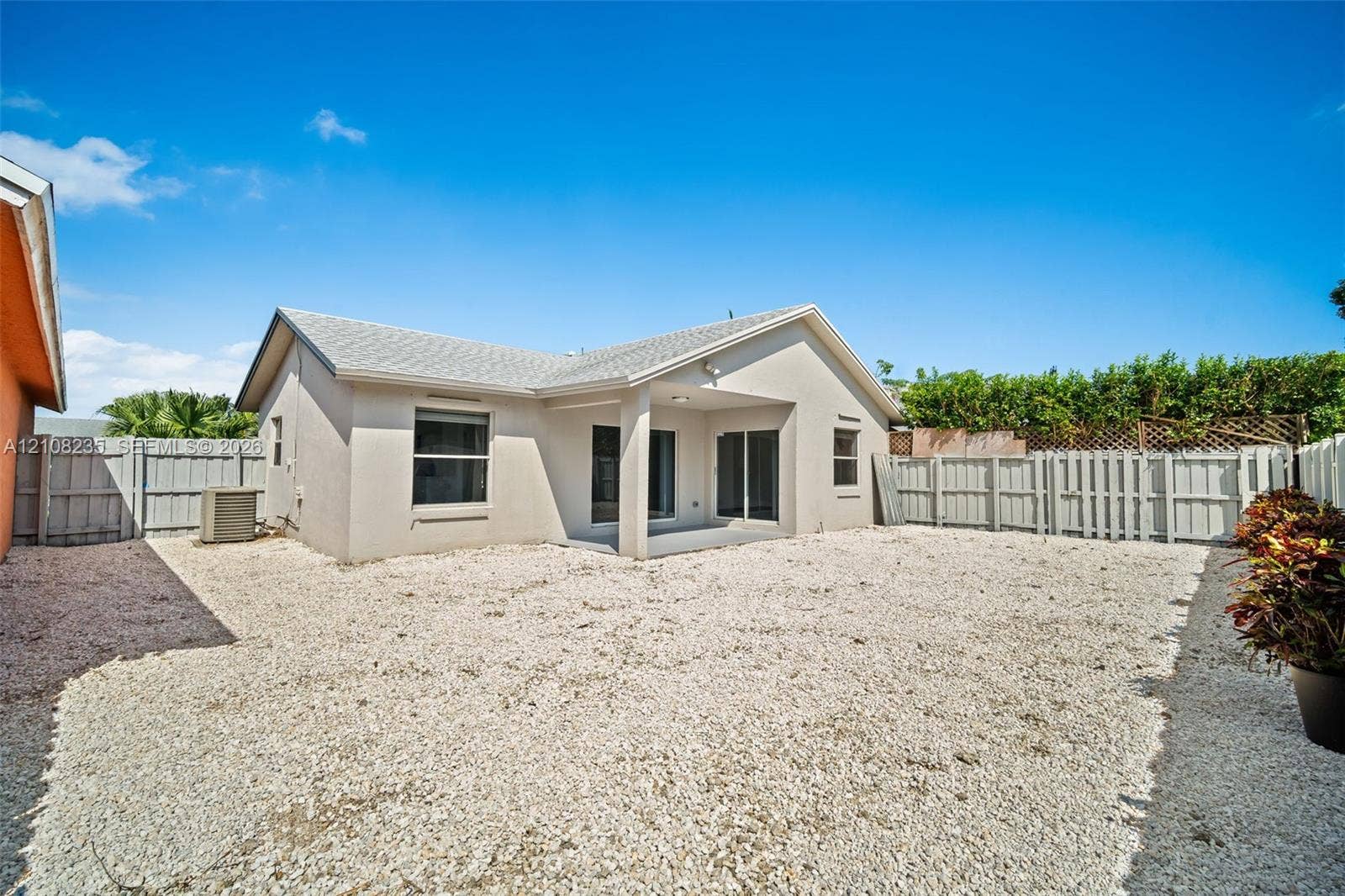 12752 SW 250th Terrace, Homestead, FL 33032 Exterior view featuring a covered patio, neutral-toned stucco siding, a gravel-surfaced yard, and privacy fencing