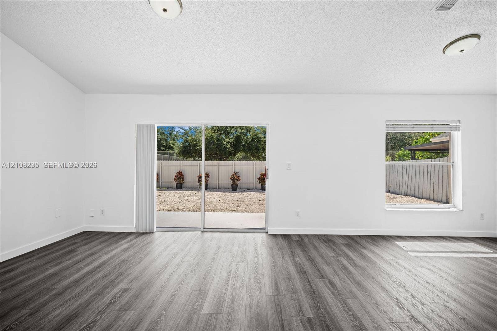 12752 SW 250th Terrace, Homestead, FL 33032 Interior space featuring wood-finish flooring, vaulted ceilings, dual flush-mount light fixtures, and a sliding glass door providing access to the rear exterior